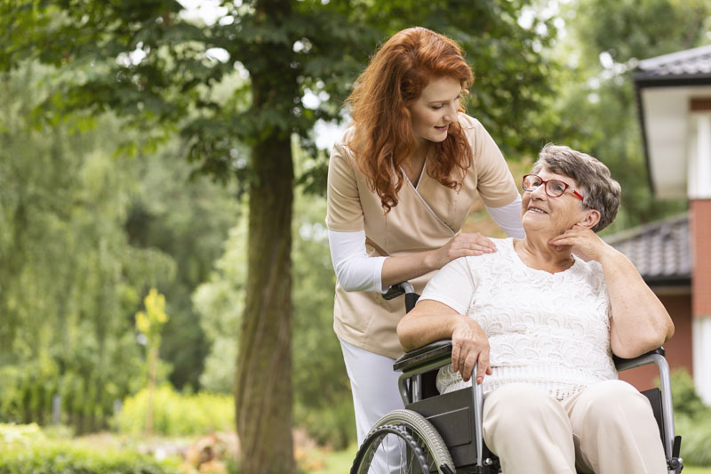 una mujer en el personal de atención domiciliaria que ayuda a una anciana en silla de ruedas