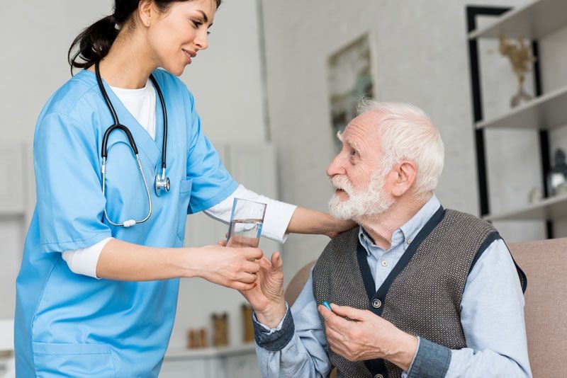 медсестра дает стакан воды пожилому мужчине с пи-LPF88XU