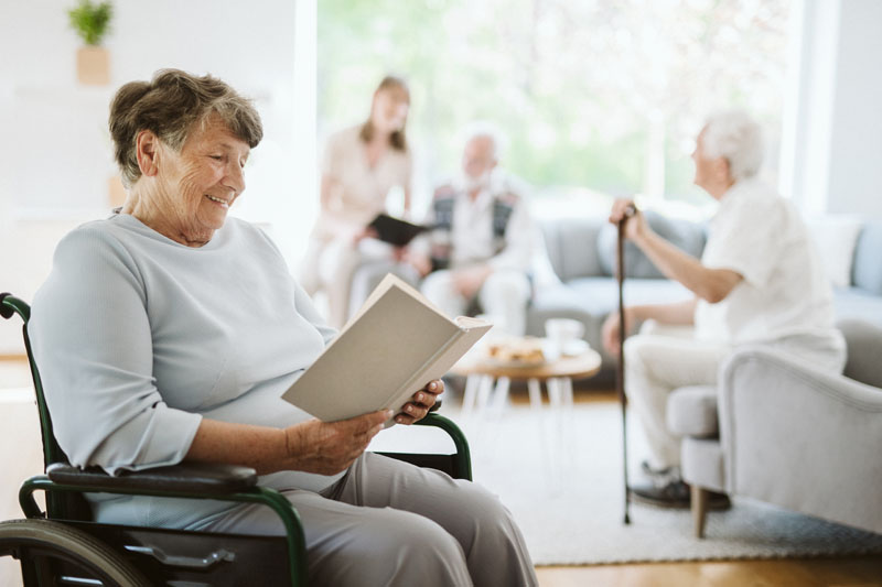 щаслива жінка-інвалід читає книгу в будинку престарілих