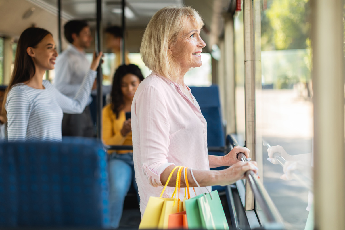 smiling mature woman taking bus holding shopping