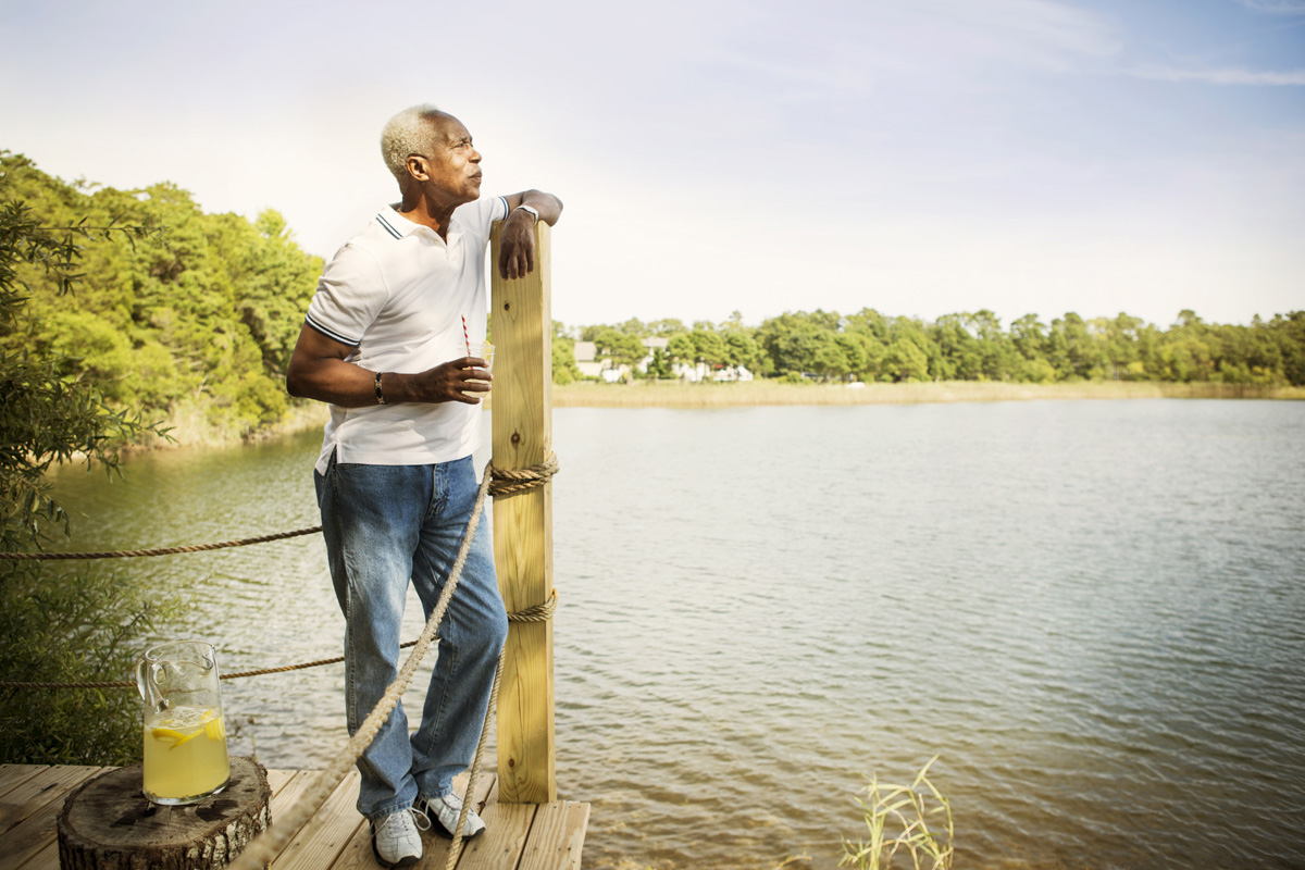 thoughtful senior man standing on pier by lake